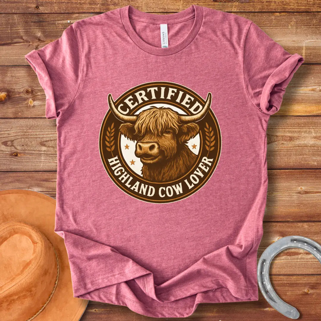 Certified Highland Cow Lover T-Shirt graphic featuring a detailed illustration of a Highland cow's head inside a circular badge.