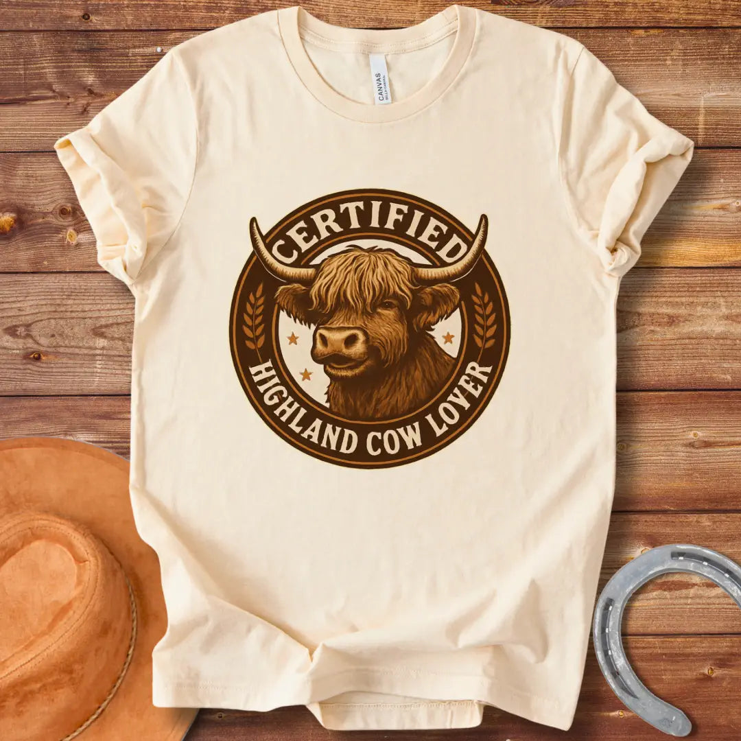 Certified Highland Cow Lover T-Shirt graphic featuring a detailed illustration of a Highland cow's head inside a circular badge.