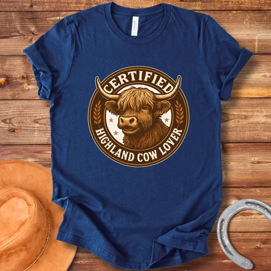 Certified Highland Cow Lover T-Shirt graphic featuring a detailed illustration of a Highland cow's head inside a circular badge.