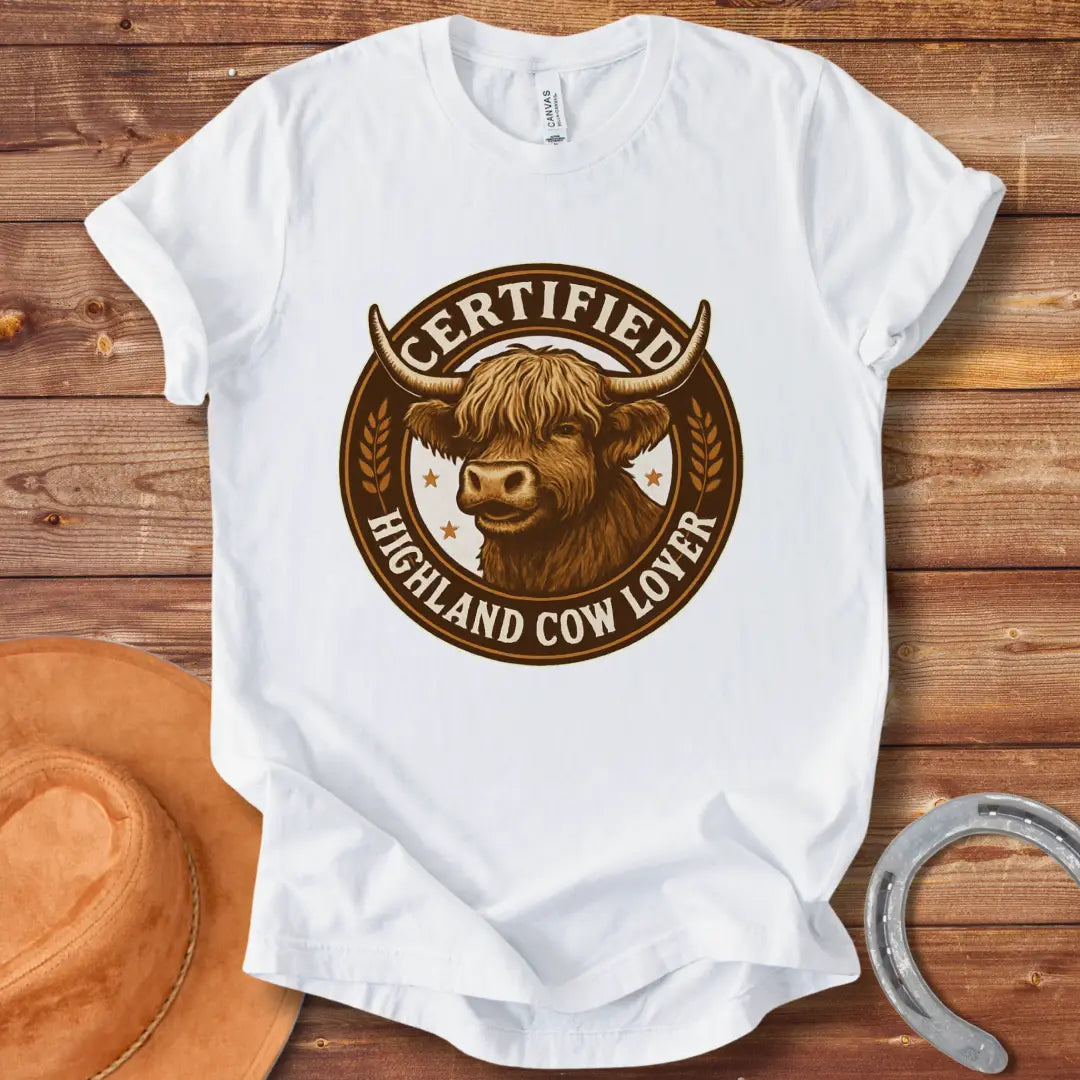Certified Highland Cow Lover T-Shirt graphic featuring a detailed illustration of a Highland cow's head inside a circular badge.