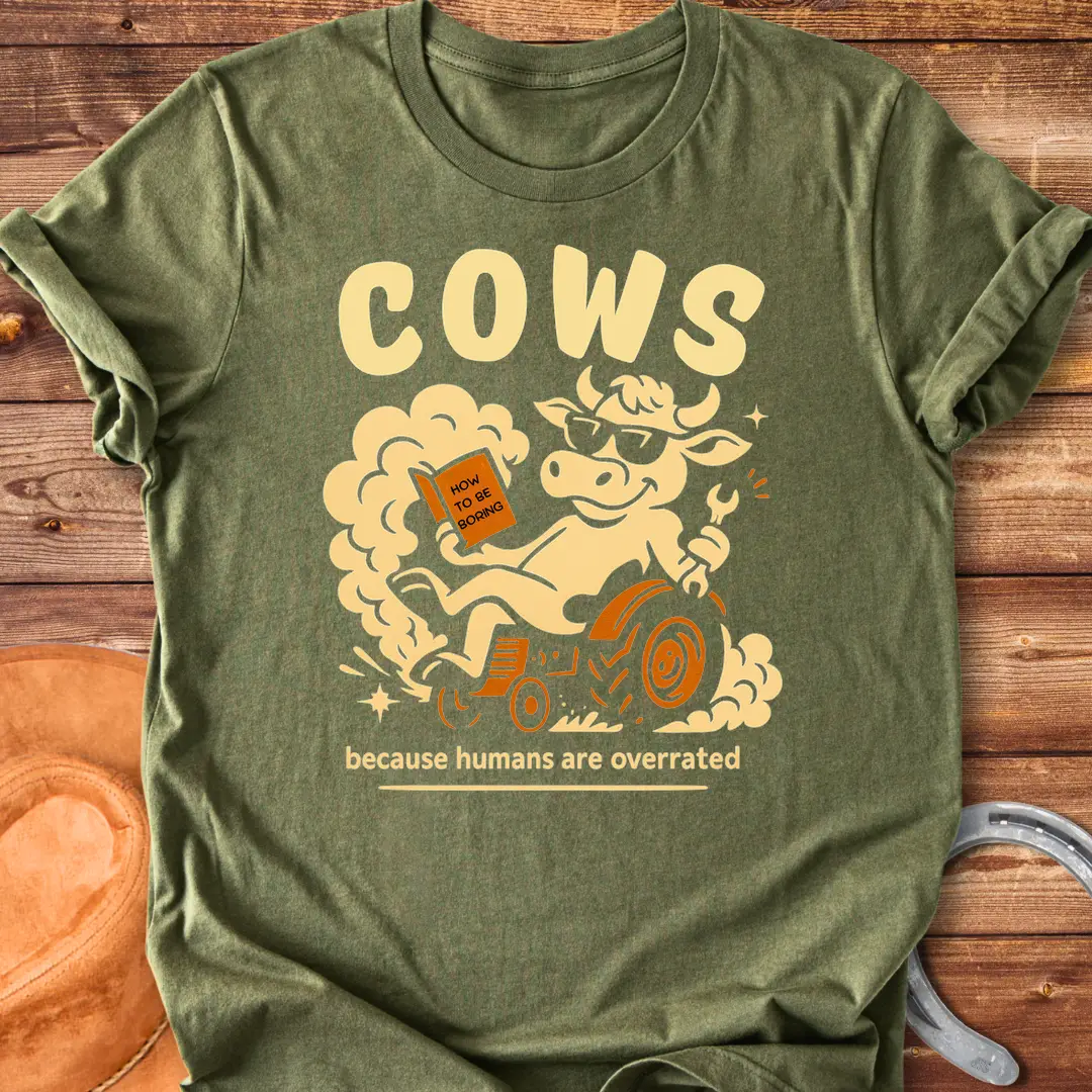 Funny t-shirt design featuring a cool cow reading a book on a tractor with the phrase 'Cows Because Humans Overrated'