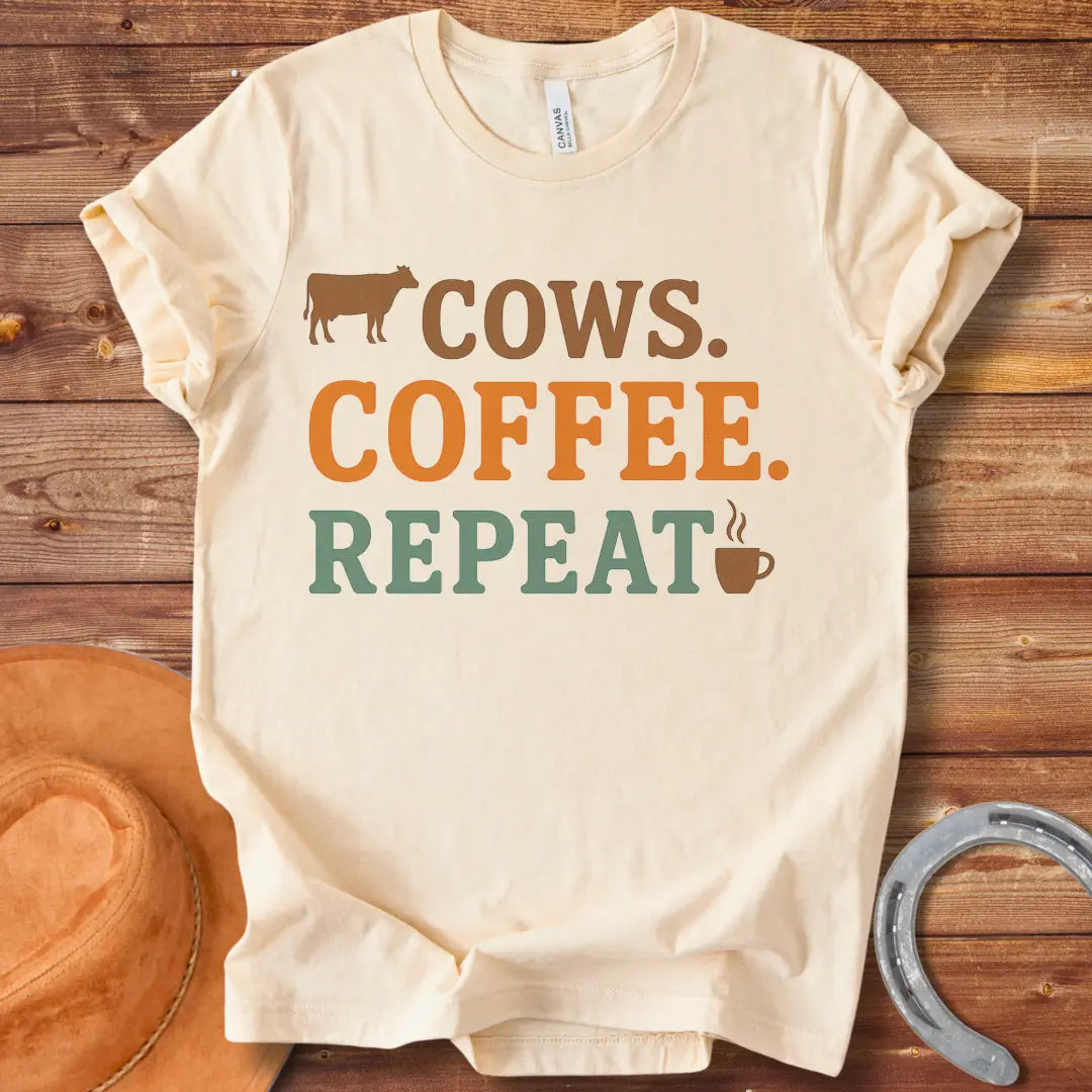 Graphic design on a t-shirt showing a cow silhouette followed by the words 'COWS. COFFEE. REPEAT.' and a coffee cup icon.