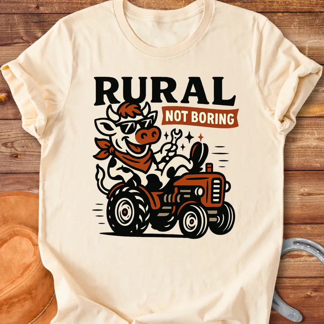 Funny t-shirt featuring a cow driving a tractor and the words 'Rural Not Boring'.