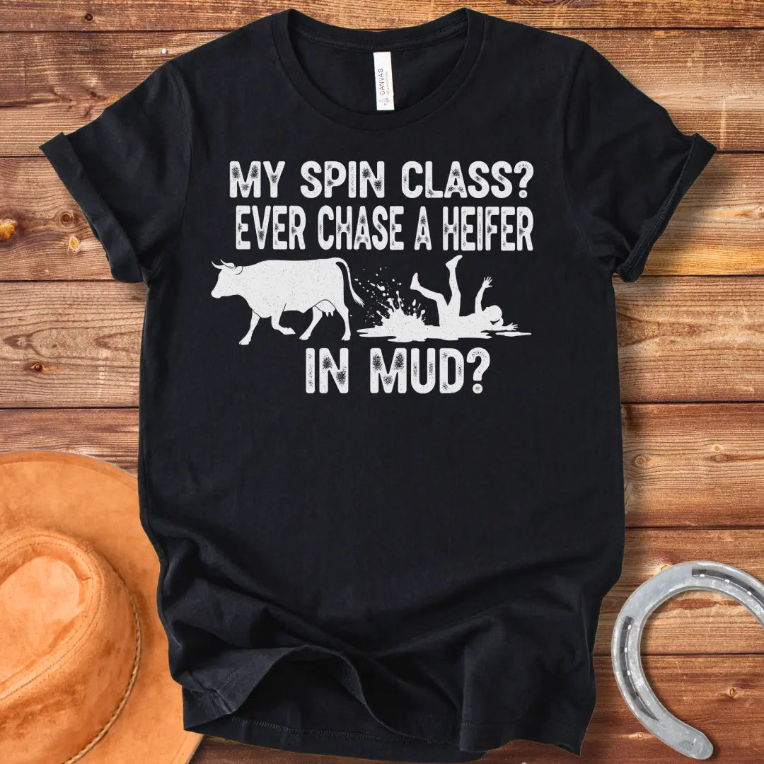 A funny illustration of a cow and a person falling in mud, with the text 'My spin class? Ever chase a heifer in mud?'
