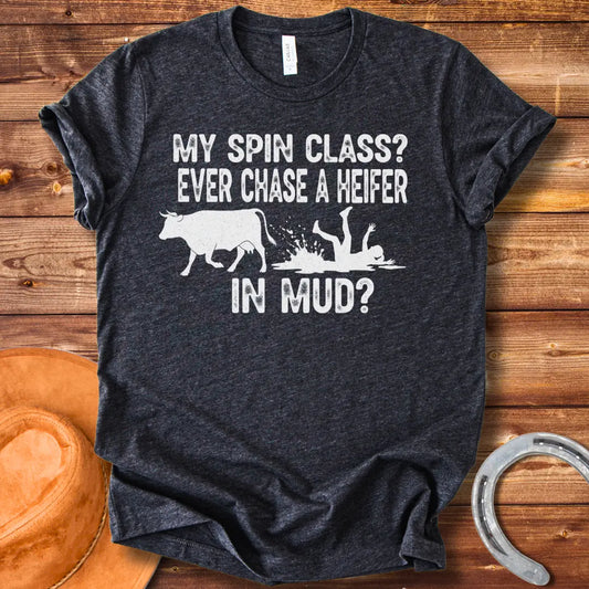 A funny illustration of a cow and a person falling in mud, with the text 'My spin class? Ever chase a heifer in mud?'