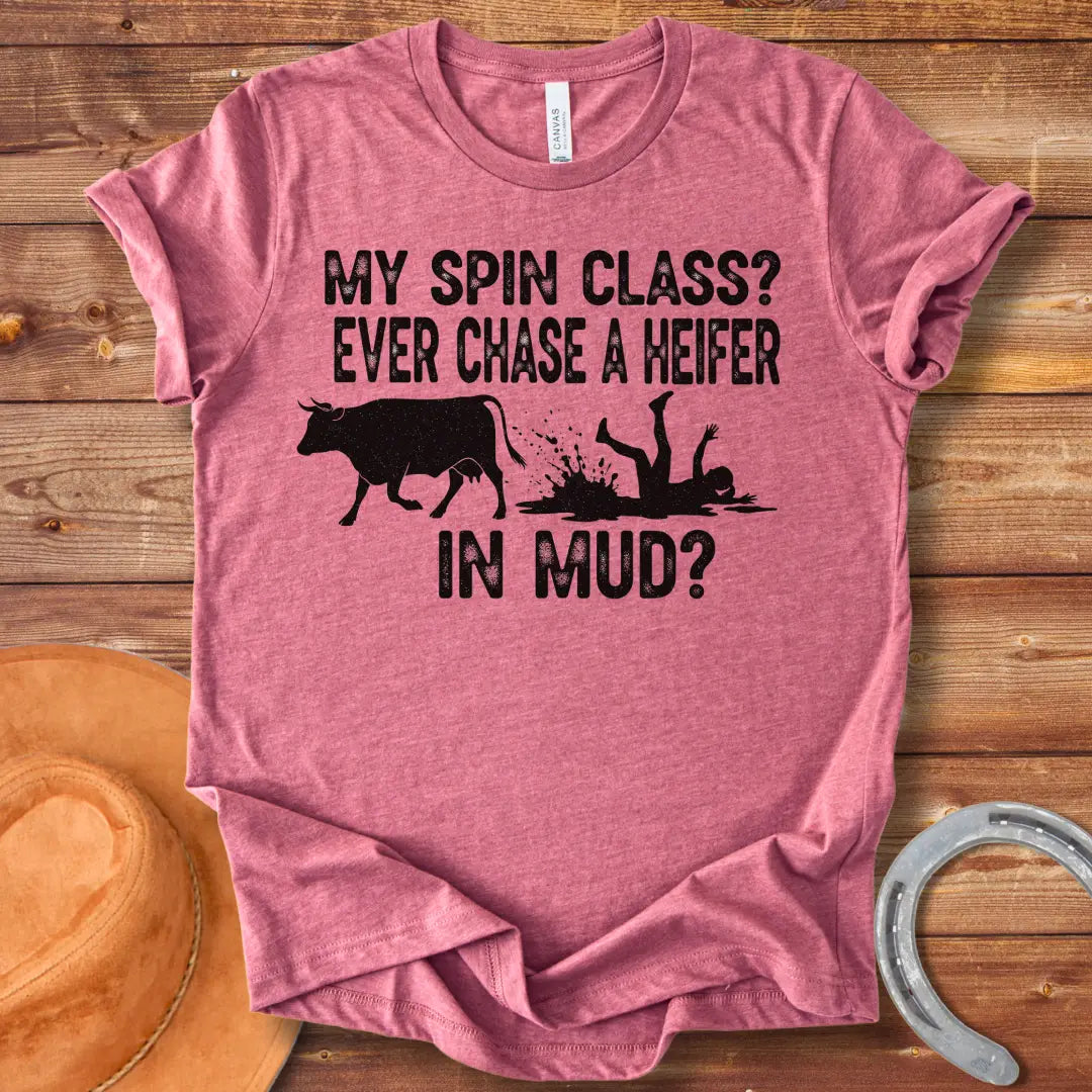 A funny illustration of a cow and a person falling in mud, with the text 'My spin class? Ever chase a heifer in mud?'