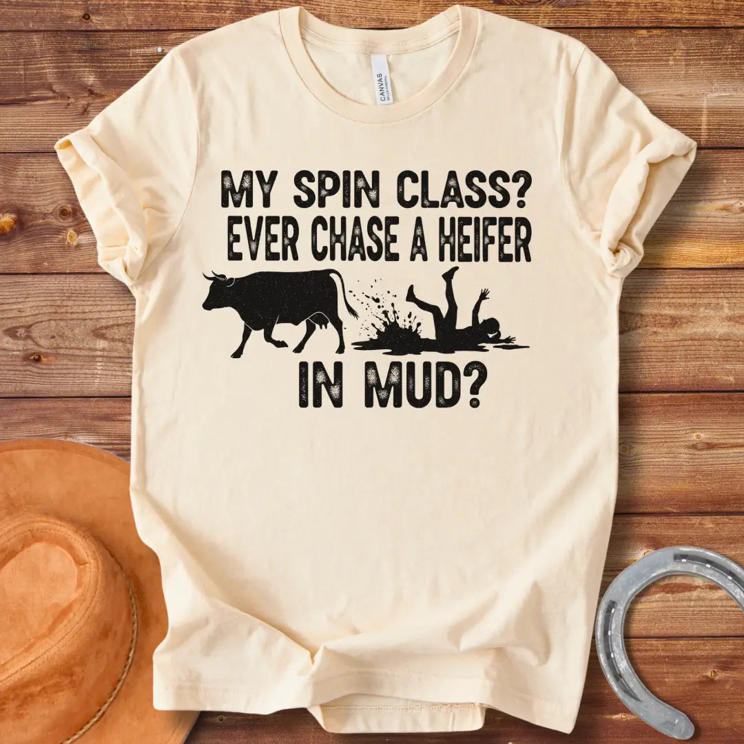 A funny illustration of a cow and a person falling in mud, with the text 'My spin class? Ever chase a heifer in mud?'