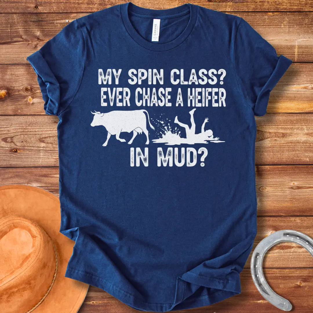 A funny illustration of a cow and a person falling in mud, with the text 'My spin class? Ever chase a heifer in mud?'