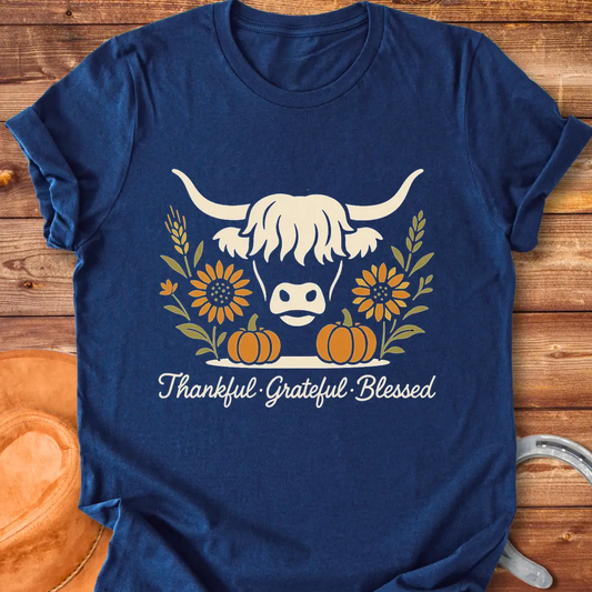 Highland cow with pumpkins, sunflower, and fall harvest design. Text reads: Thankful, Grateful, Blessed. Cow Lovers Clothing.