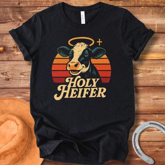 Holy Heifer T-Shirt from Cow Lovers Clothing, featuring a smiling cow with a halo and the text 'Holy Heifer' with a sunset background.