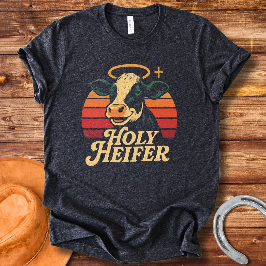Holy Heifer T-Shirt from Cow Lovers Clothing, featuring a smiling cow with a halo and the text 'Holy Heifer' with a sunset background.