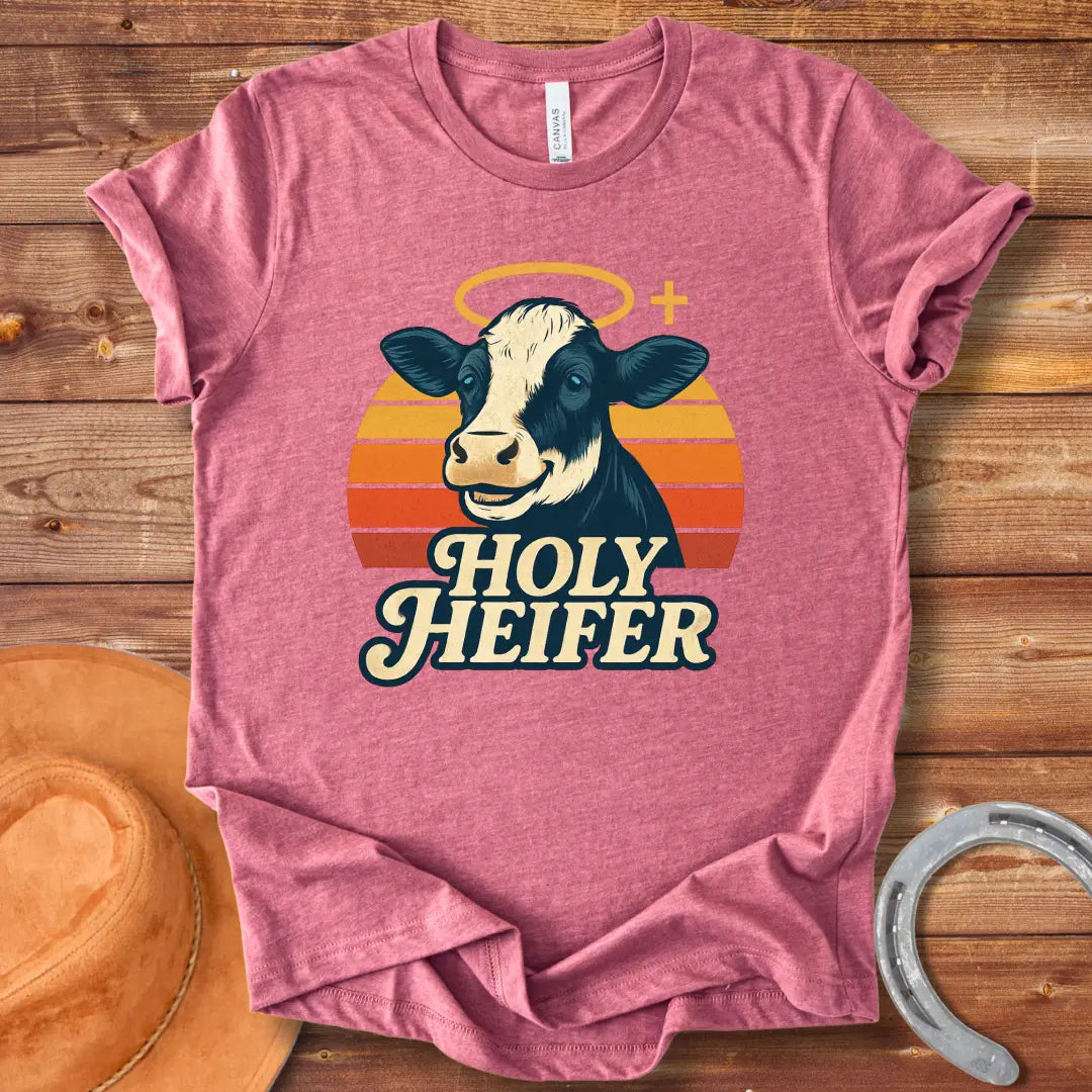 Holy Heifer T-Shirt from Cow Lovers Clothing, featuring a smiling cow with a halo and the text 'Holy Heifer' with a sunset background.