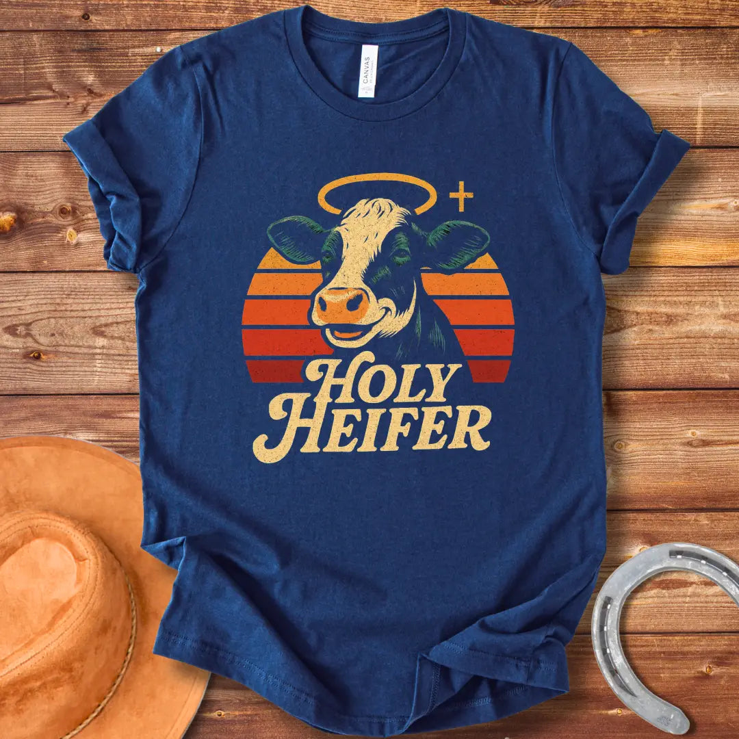 Holy Heifer T-Shirt from Cow Lovers Clothing, featuring a smiling cow with a halo and the text 'Holy Heifer' with a sunset background.