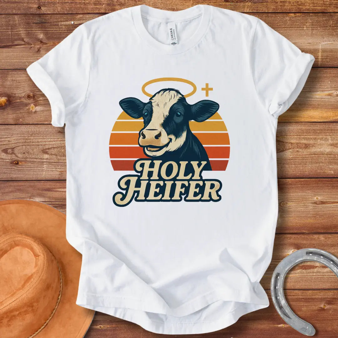 Holy Heifer T-Shirt from Cow Lovers Clothing, featuring a smiling cow with a halo and the text 'Holy Heifer' with a sunset background.