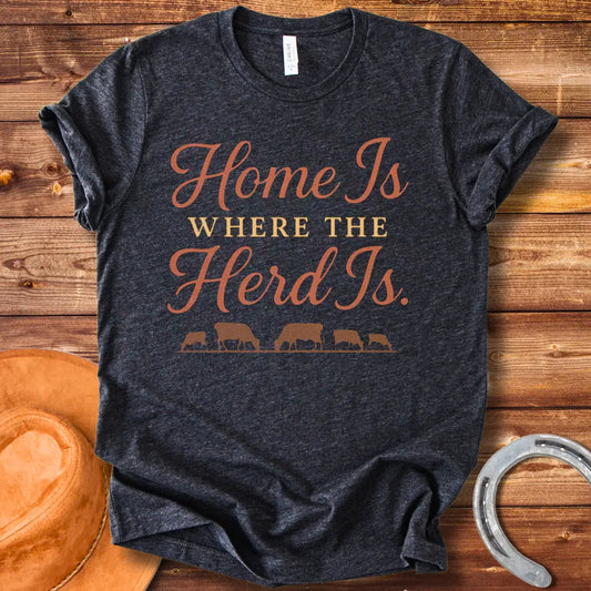 Orange text on a black t-shirt that says, "Home Is Where The Herd Is." Below the text is a silhouette of a herd of cows grazing.