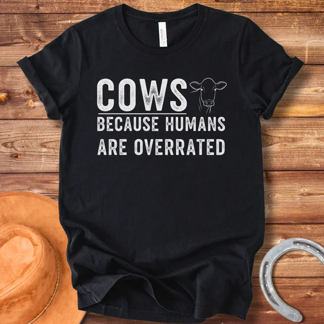 A black and white graphic t-shirt design that reads 'COWS BECAUSE HUMANS ARE OVERRATED' with a simple cow illustration.