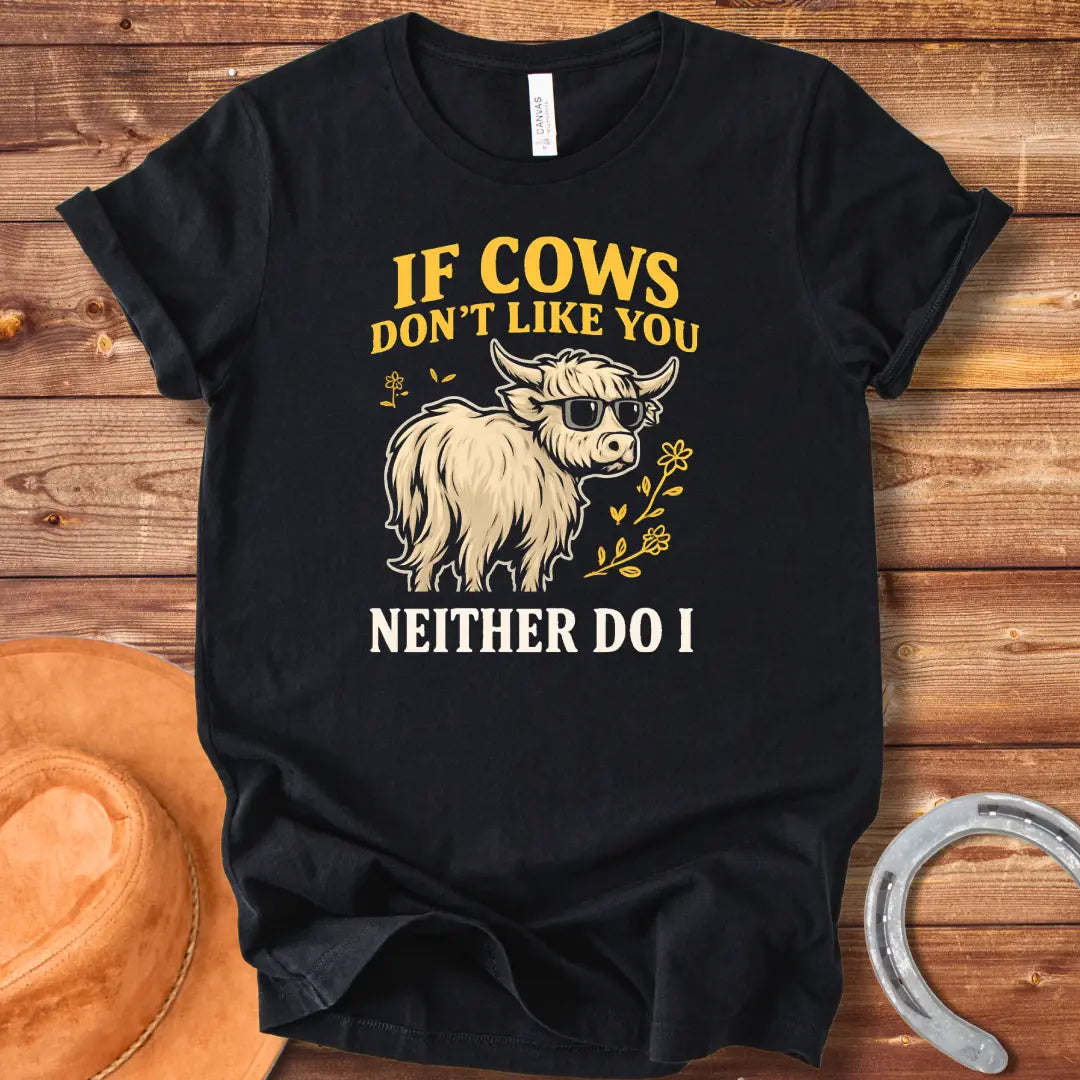 T-shirt design featuring a cool cow wearing sunglasses with the text 'If Cows Don't Like You Neither Do I' in brown and blue font on a black background.