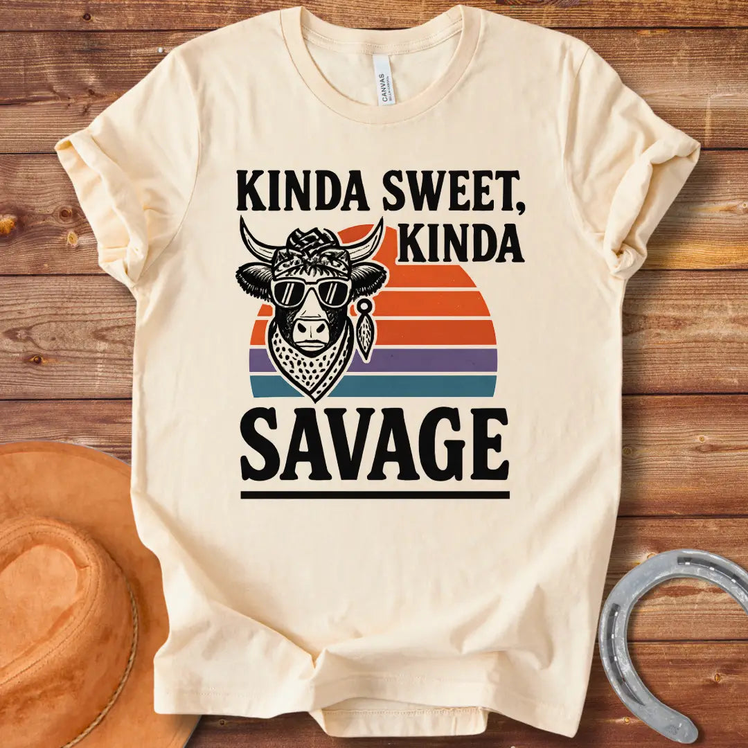 Vintage t-shirt featuring a cool cow wearing sunglasses and a bandana with the text 'Kinda Sweet Kinda Savage' over a retro sunset background.