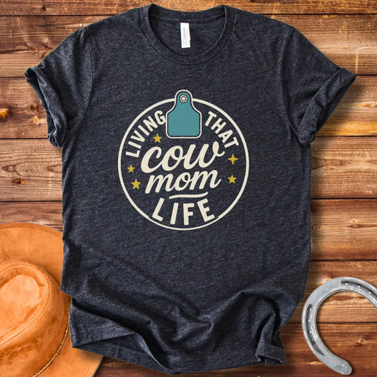A round design featuring the text 'Living That Cow Mom Life' surrounding a cow tag graphic with orange stars.