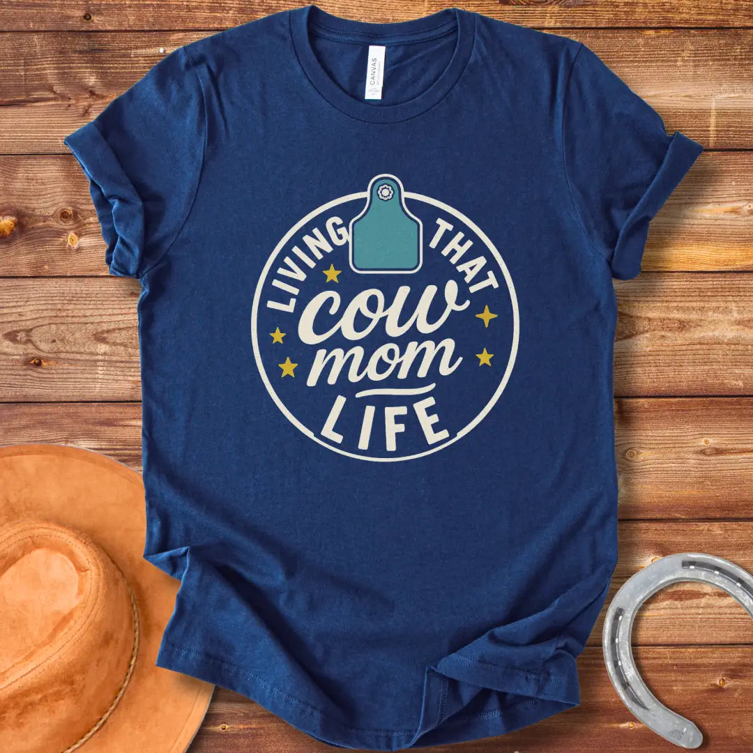 A round design featuring the text 'Living That Cow Mom Life' surrounding a cow tag graphic with orange stars.