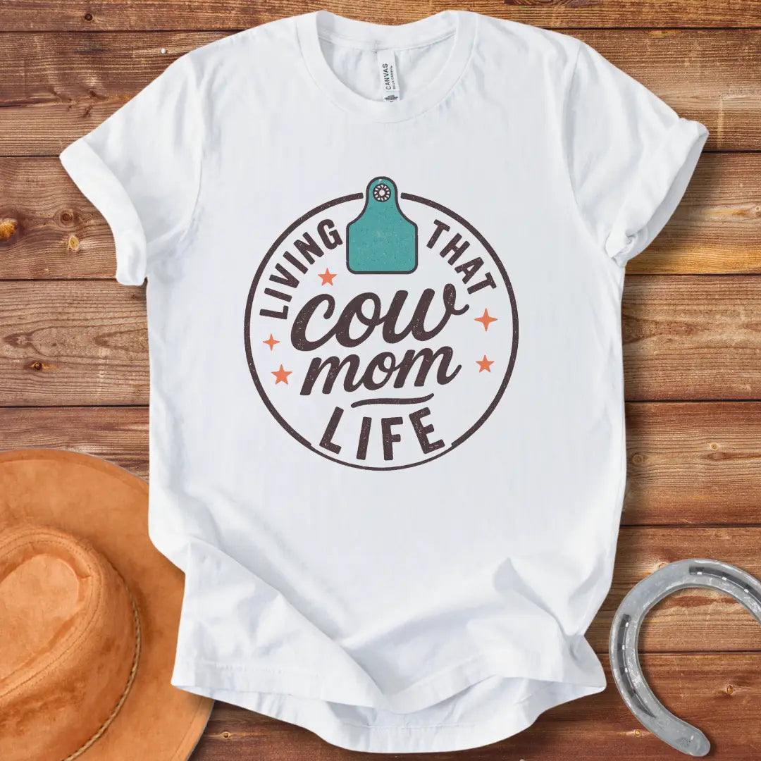 A round design featuring the text 'Living That Cow Mom Life' surrounding a cow tag graphic with orange stars.