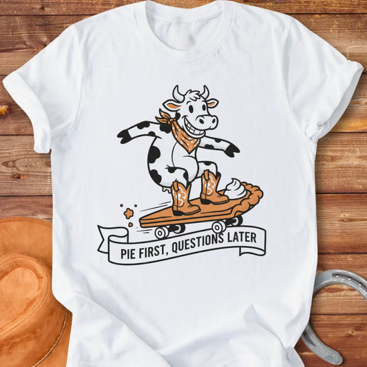 T-shirt design featuring a cow riding a pie skateboard with the words 'Pie First, Questions Later'.