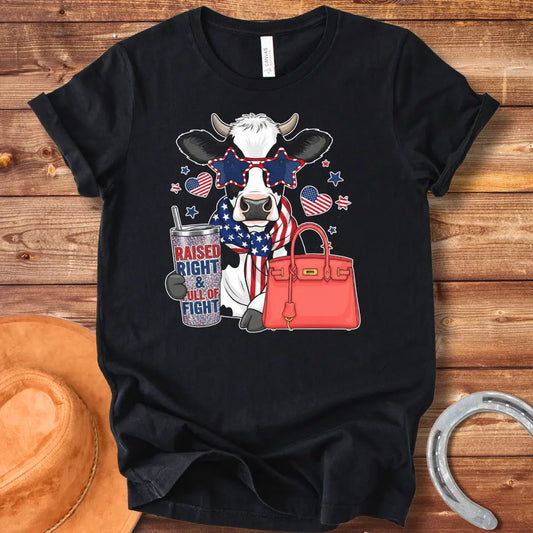 Patriotic cow t-shirt. Cow wearing star-shaped sunglasses, American flag scarf, and holding a tumbler that says 'Raised Right & Full of Fight', with a red purse.