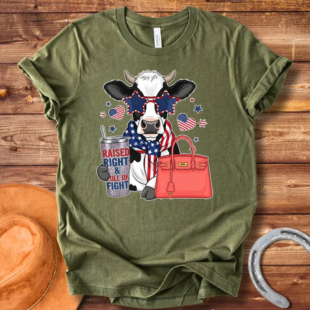 Patriotic cow t-shirt. Cow wearing star-shaped sunglasses, American flag scarf, and holding a tumbler that says 'Raised Right & Full of Fight', with a red purse.