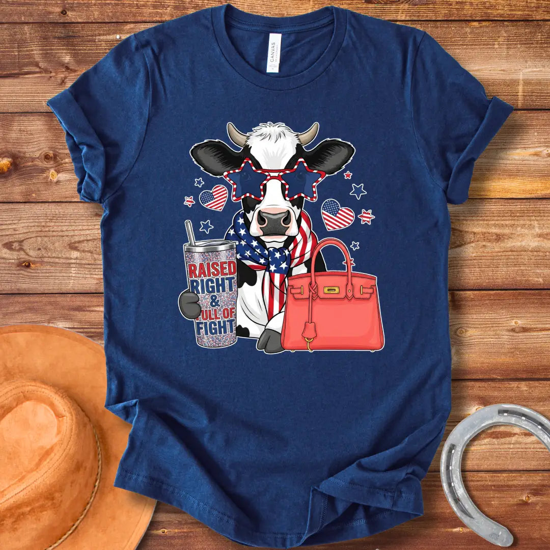 Patriotic cow t-shirt. Cow wearing star-shaped sunglasses, American flag scarf, and holding a tumbler that says 'Raised Right & Full of Fight', with a red purse.