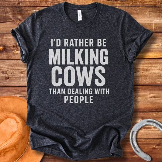 A black and white graphic t-shirt design with the text 'I'd rather be milking cows than dealing with people'.