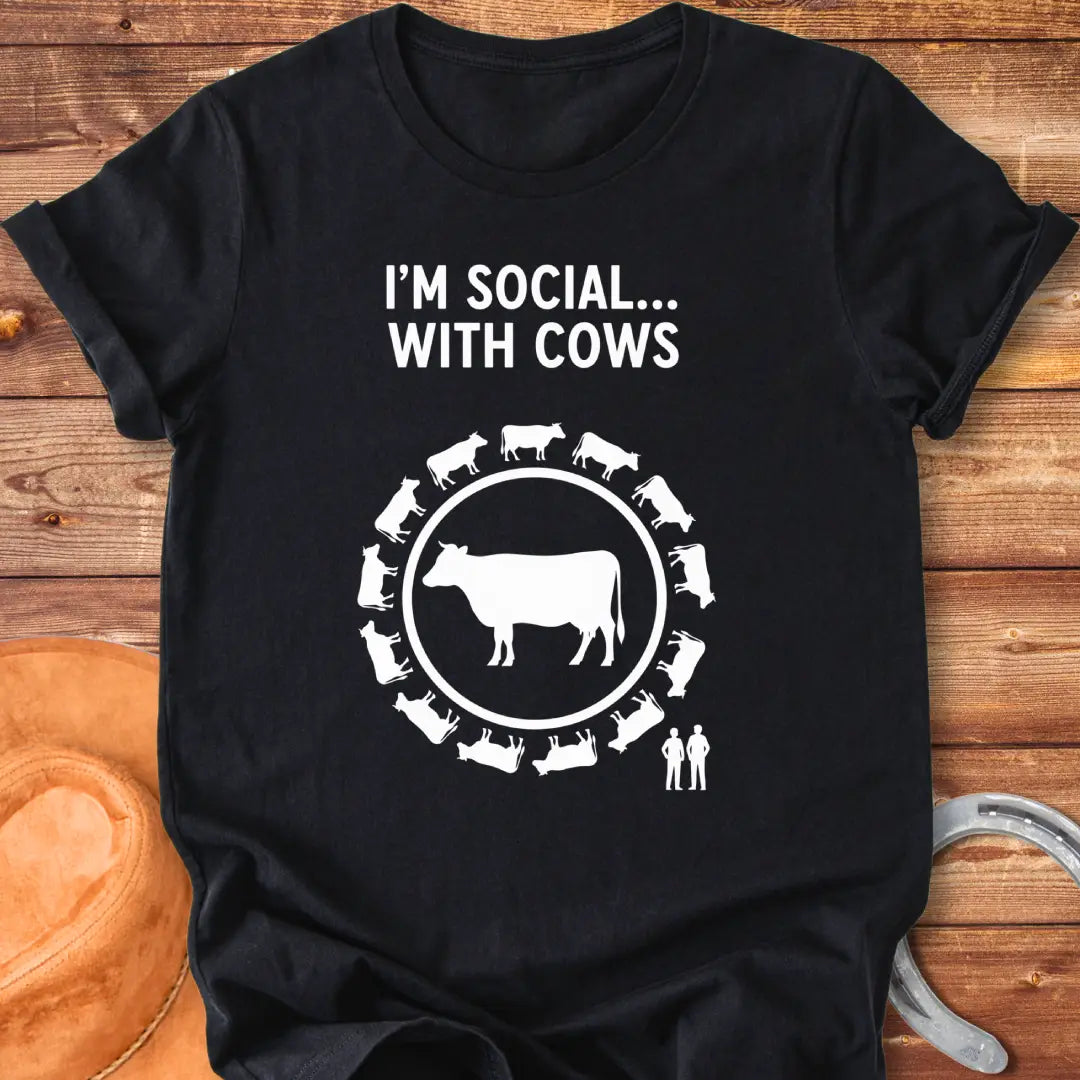 Black and white t-shirt design featuring a cow surrounded by smaller cow silhouettes with the words 'I'm social... with cows' above.