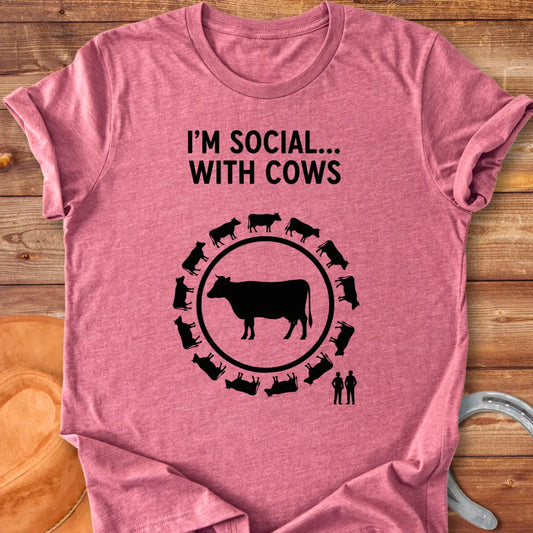Black and white t-shirt design featuring a cow surrounded by smaller cow silhouettes with the words 'I'm social... with cows' above.