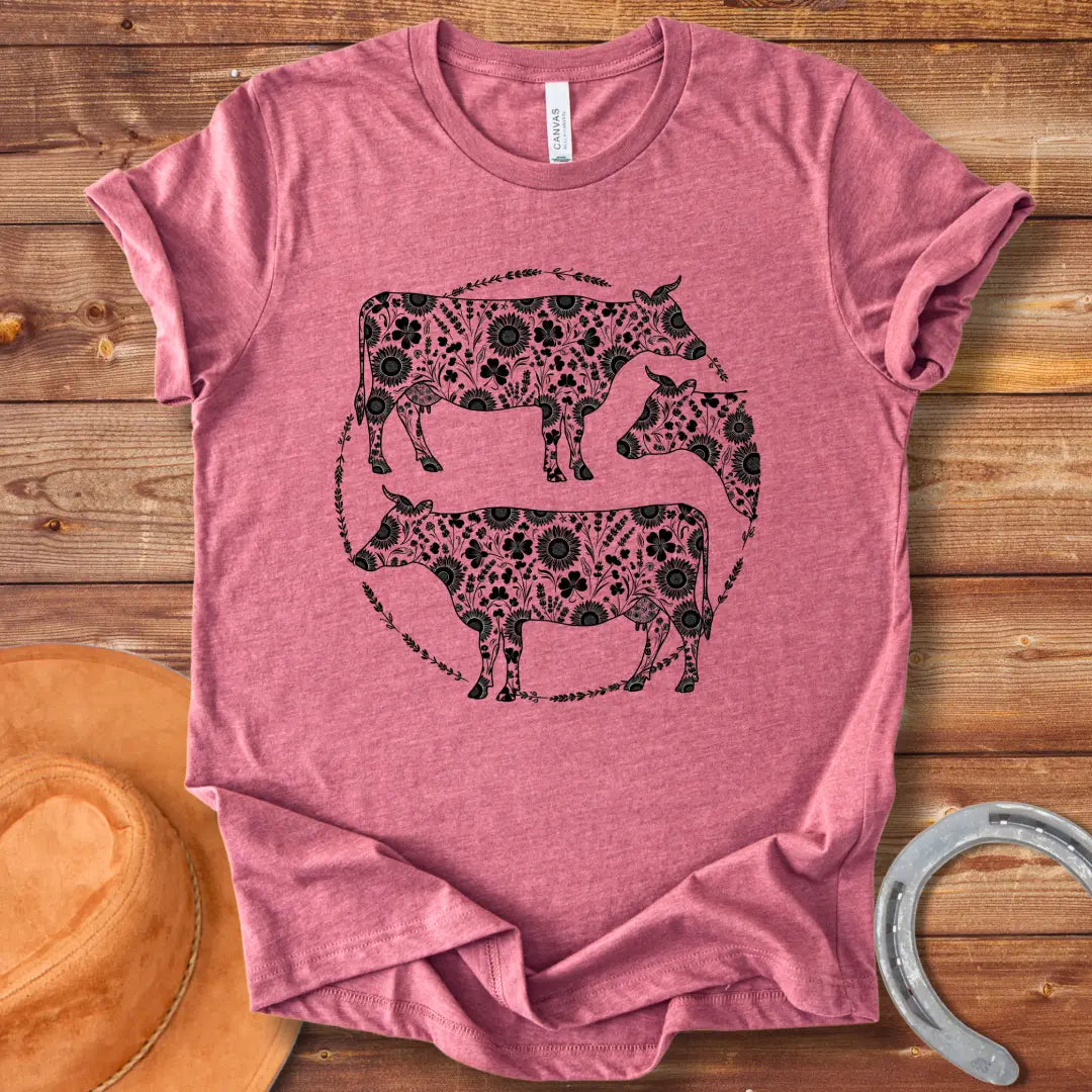 Black and white illustration of three cows with floral patterns within a circle.