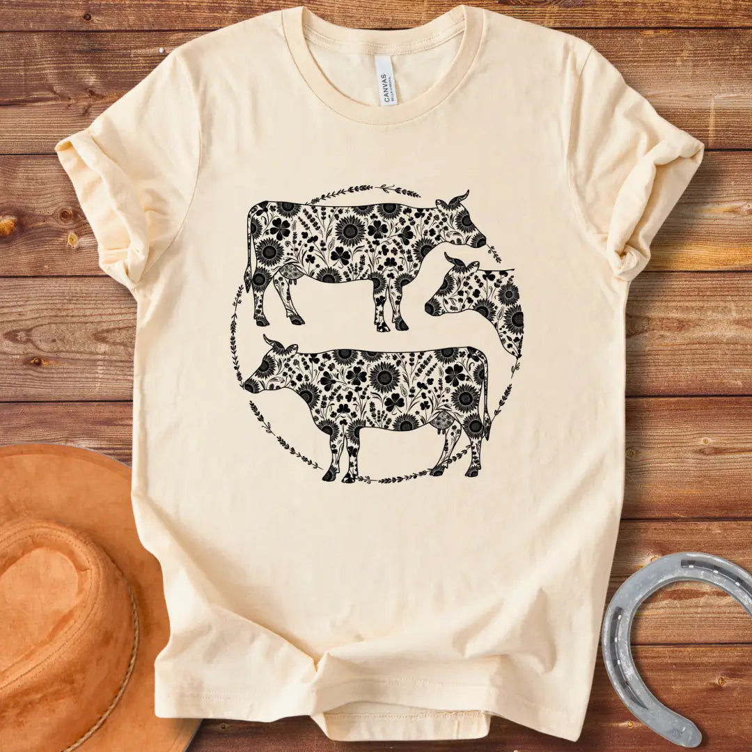 Black and white illustration of three cows with floral patterns within a circle.