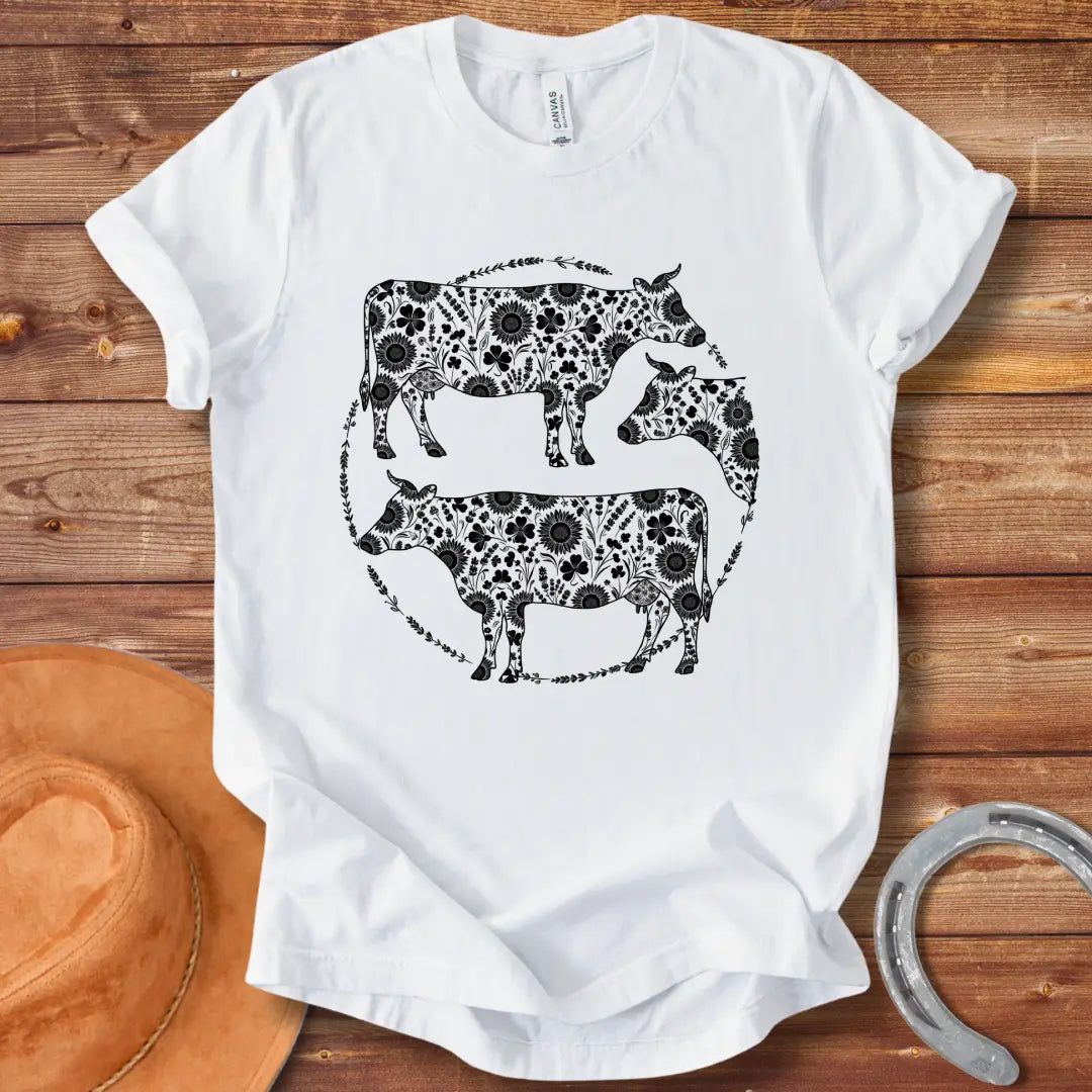 Black and white illustration of three cows with floral patterns within a circle.