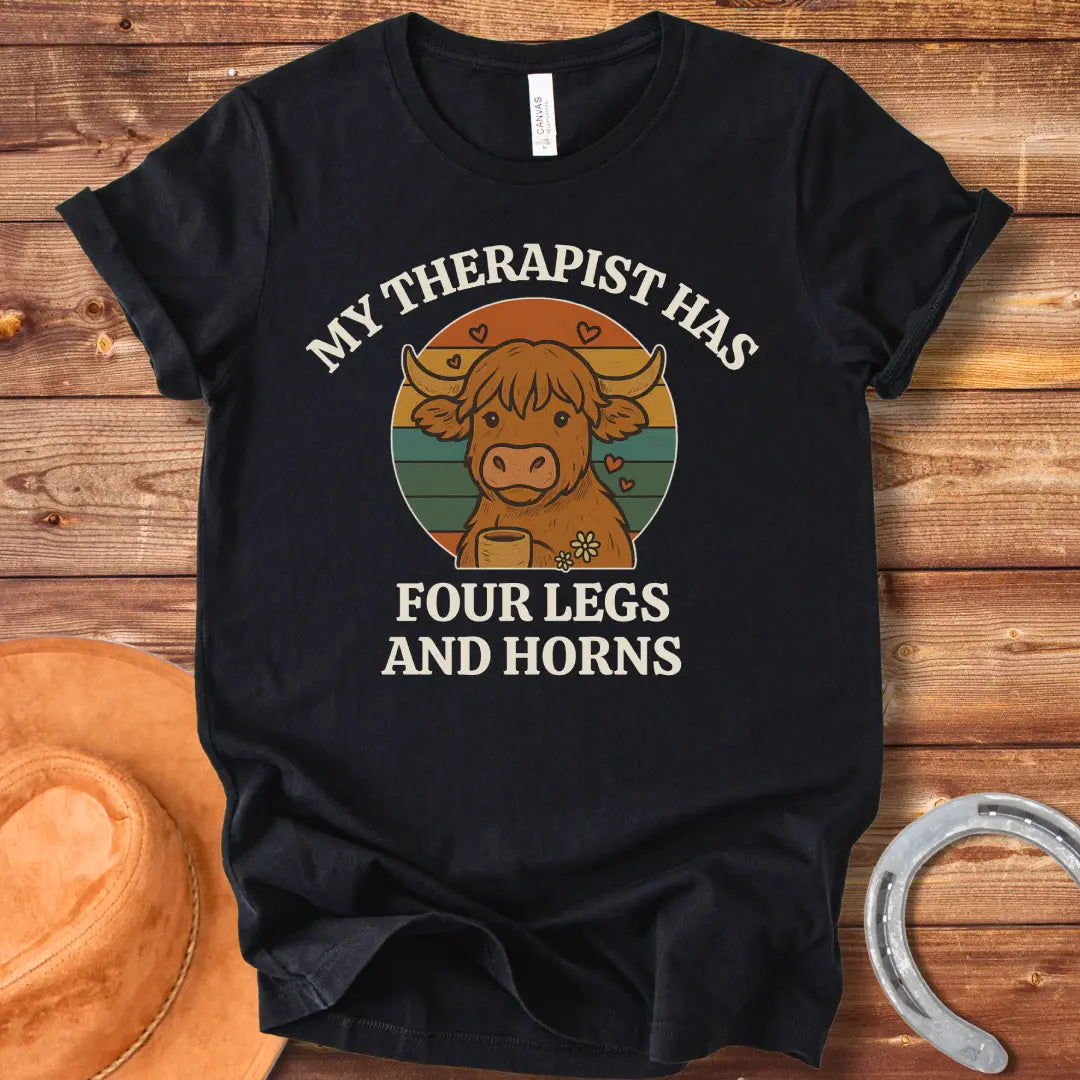 T-shirt design featuring a cartoon Highland cow with the text 'My Therapist Has Four Legs and Horns'.