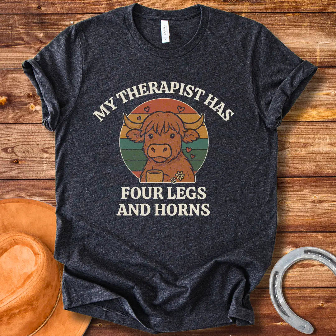 T-shirt design featuring a cartoon Highland cow with the text 'My Therapist Has Four Legs and Horns'.