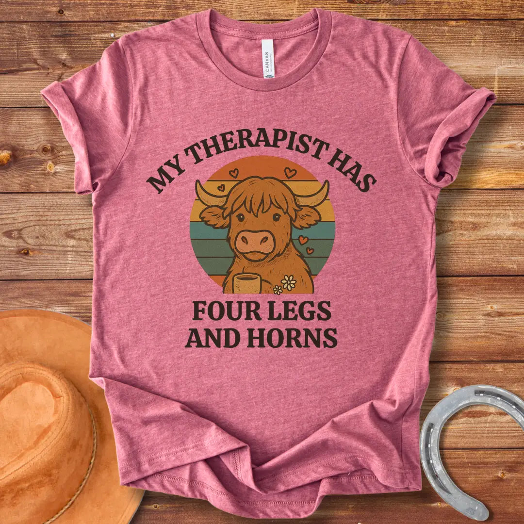 T-shirt design featuring a cartoon Highland cow with the text 'My Therapist Has Four Legs and Horns'.