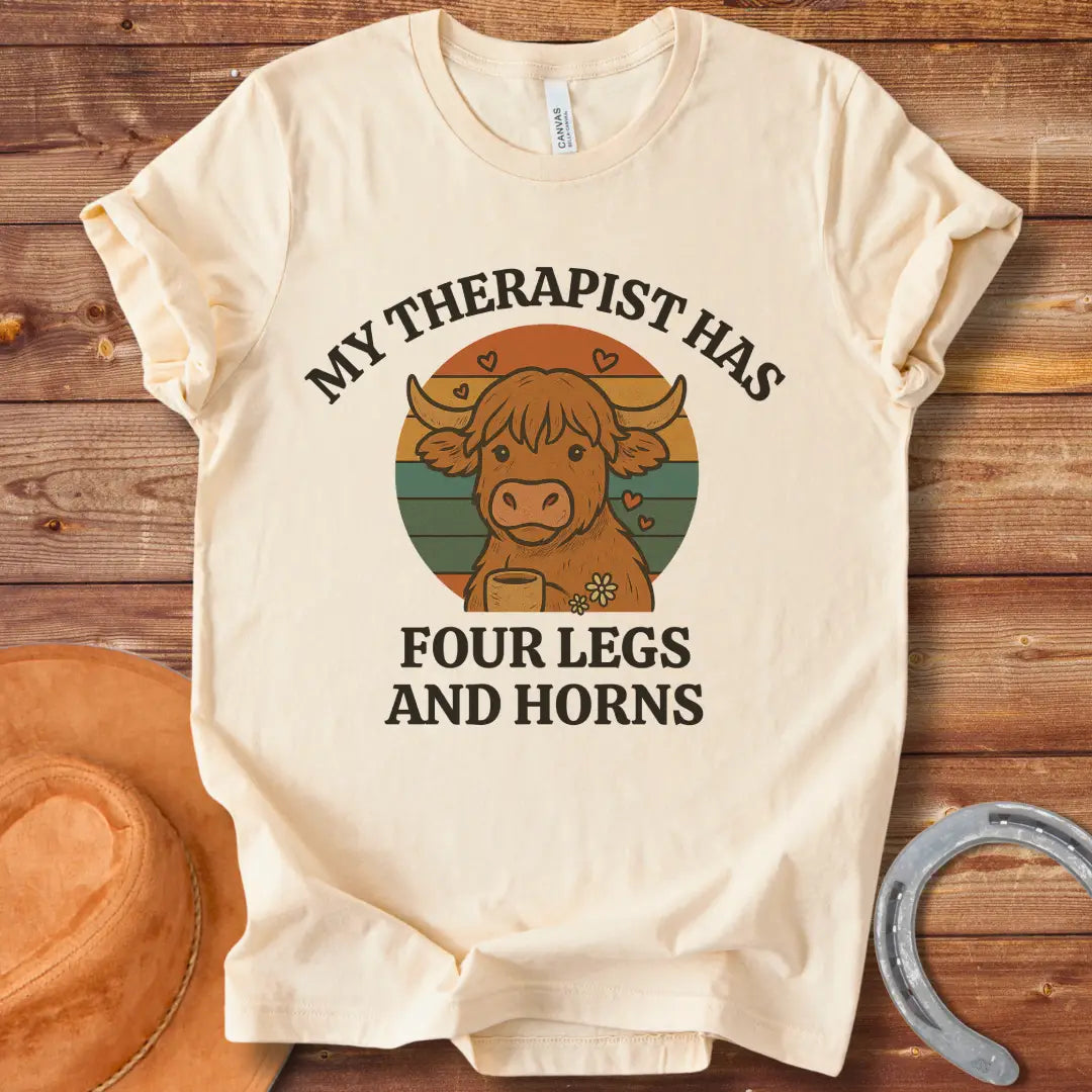 T-shirt design featuring a cartoon Highland cow with the text 'My Therapist Has Four Legs and Horns'.