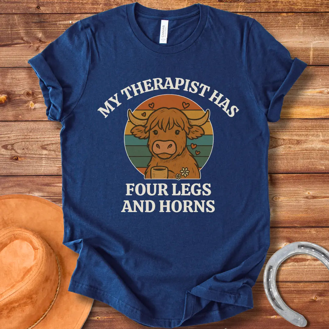 T-shirt design featuring a cartoon Highland cow with the text 'My Therapist Has Four Legs and Horns'.