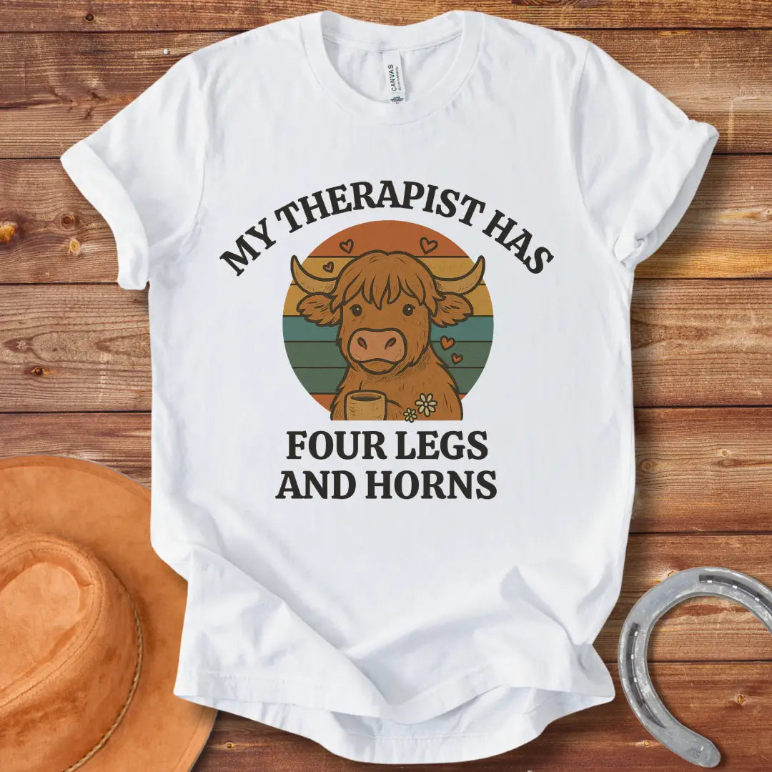 T-shirt design featuring a cartoon Highland cow with the text 'My Therapist Has Four Legs and Horns'.